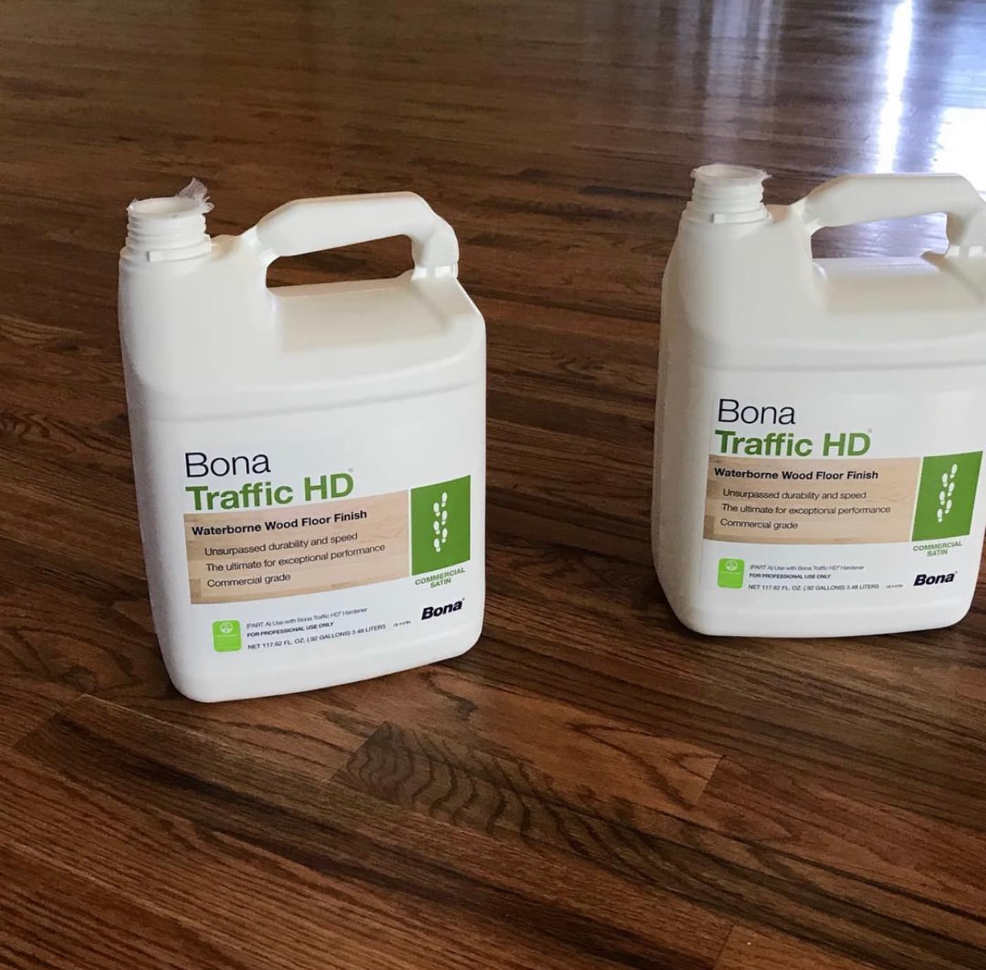 Two jugs of Bona Traffic HD Part A on a finished red oak floor, labeled for use with Bona Traffic HD Hardener