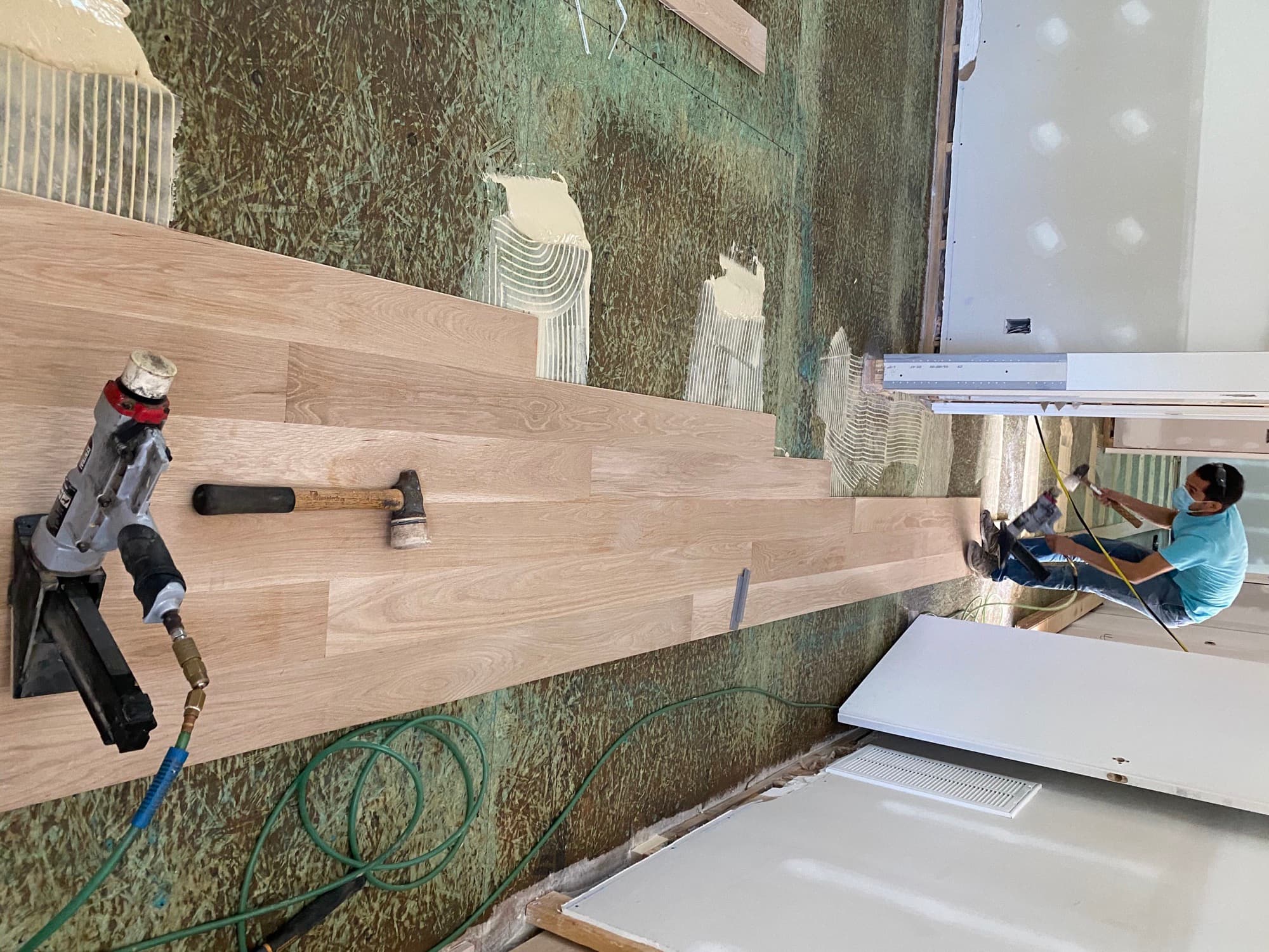 Glue-and-nail installation of wide plank white oak flooring in progress over a plywood subfloor with adhesive troweled ahead of the boards