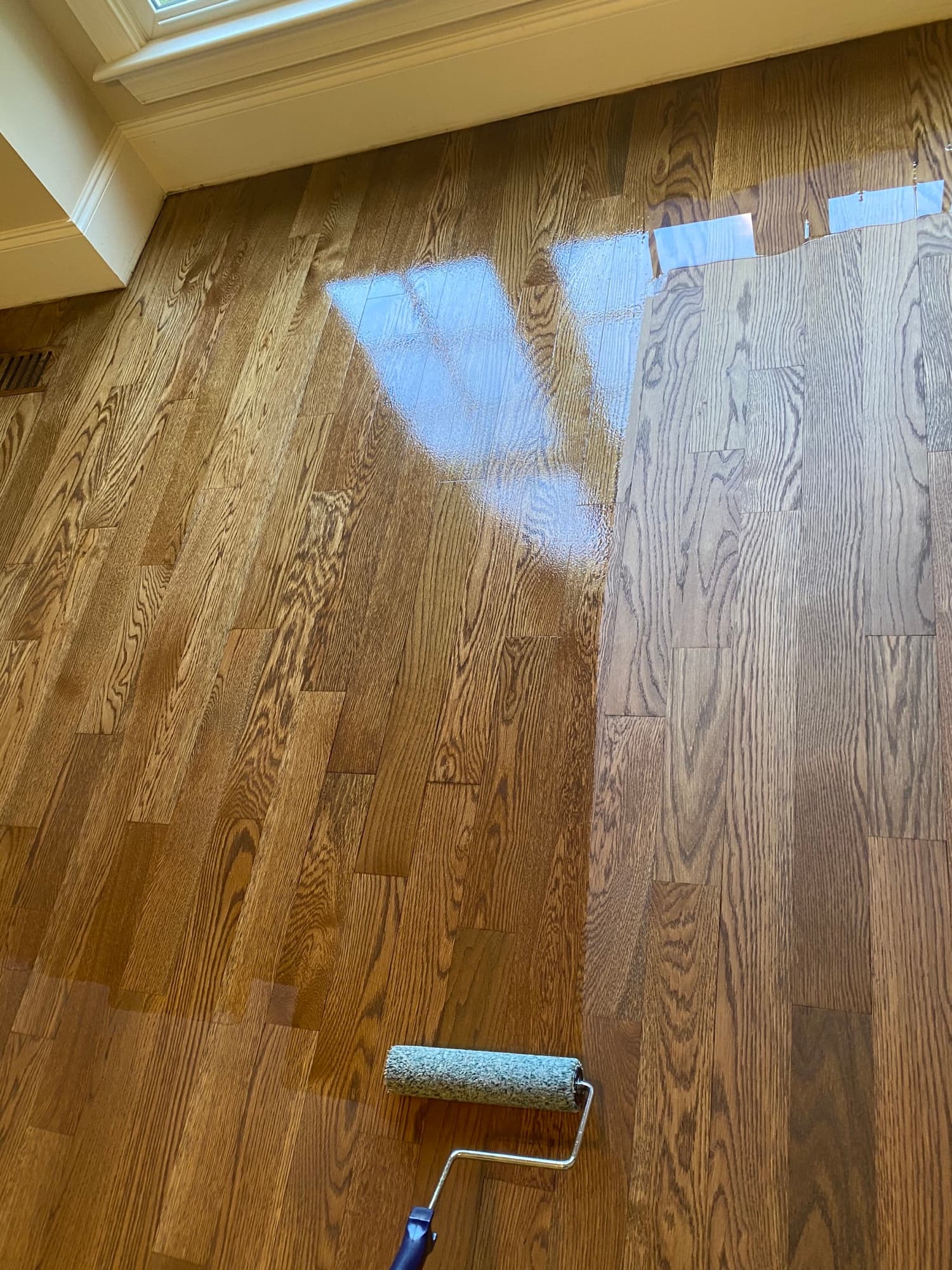 Fresh coat of finish applied with a roller during a hardwood floor recoat on red oak