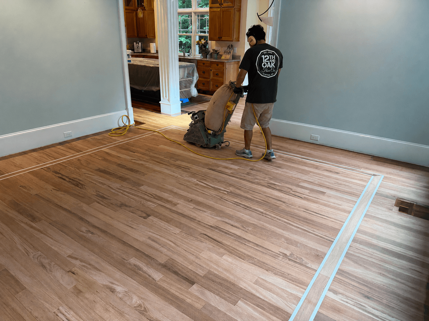 12th And Oak technician operating drum sander on hardwood floor during refinishing project NC
