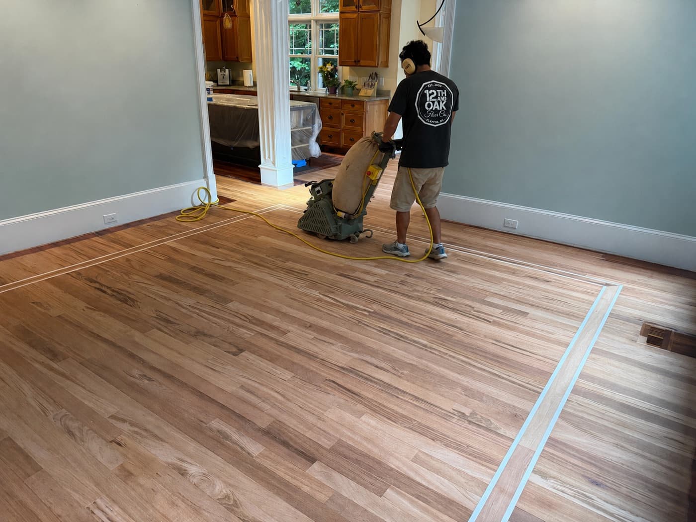 12th And Oak crew rough sanding raw Brazilian Tigerwood floor with planetary sander, maple inlay borders exposed, in Glen Laurel Clayton NC