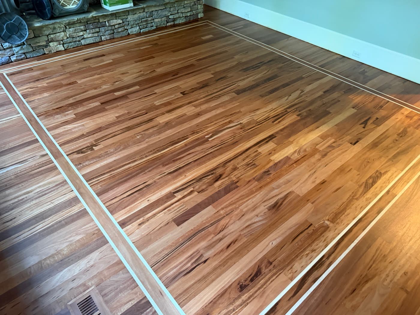 Finished Brazilian Tigerwood floor with maple inlay border at stone fireplace in Glen Laurel Clayton NC