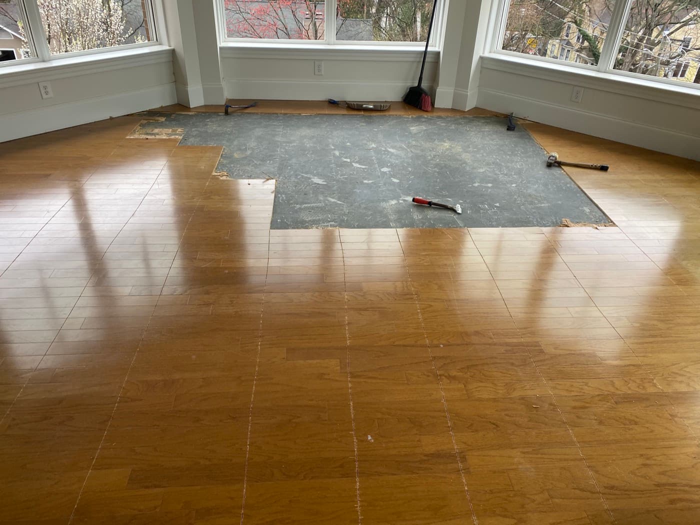 Living room with existing engineered hardwood removed, dark adhesive mastic visible on concrete slab
