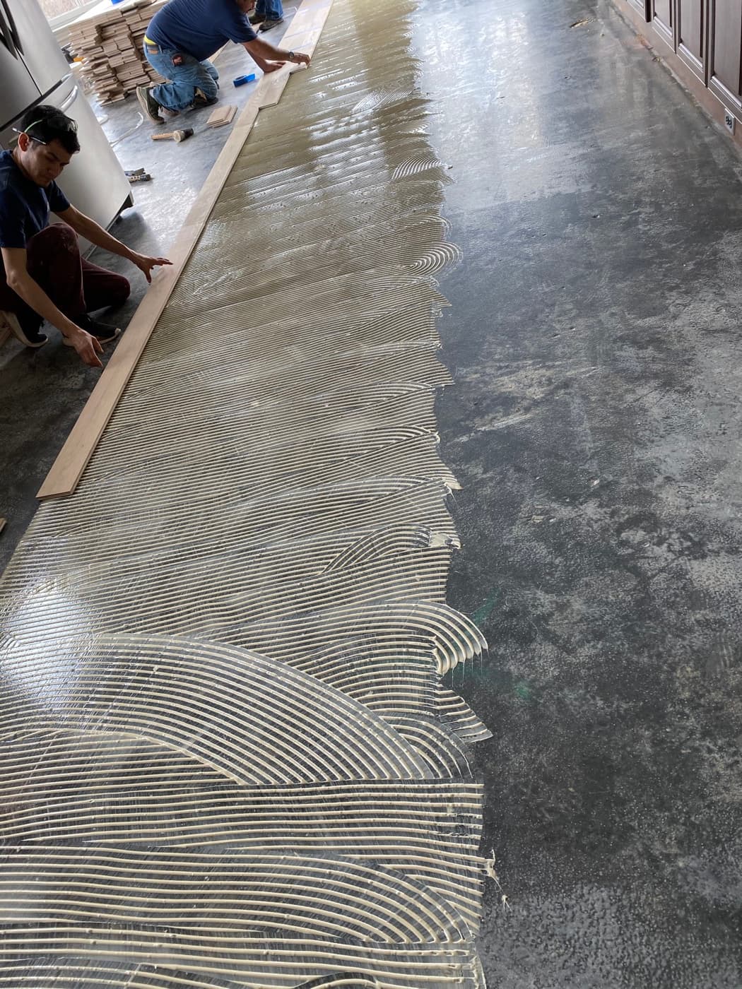 Workers spreading adhesive on concrete subfloor for glue-down engineered hardwood installation