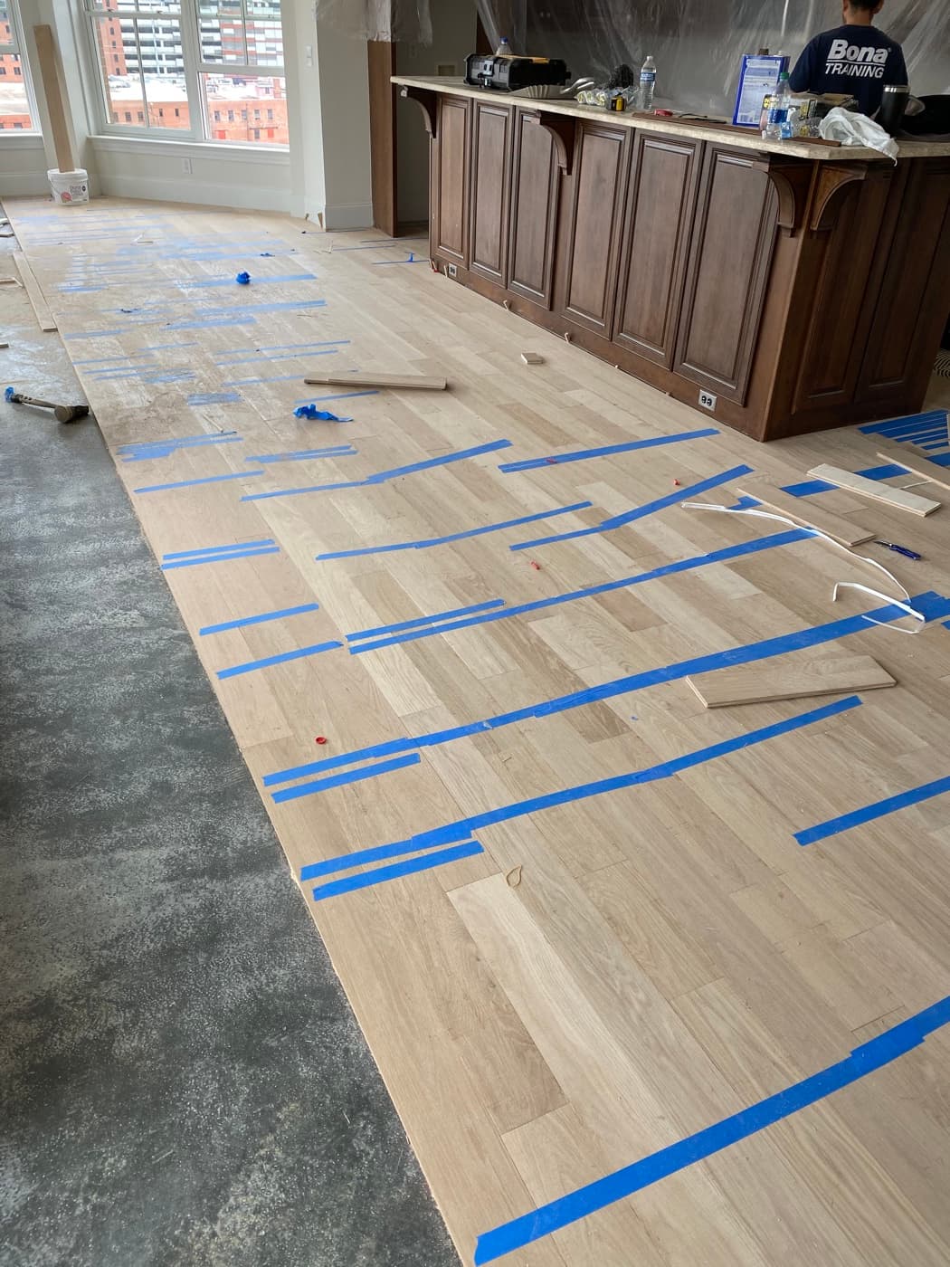 5" engineered white oak boards being laid glue-down with blue tape holding seams