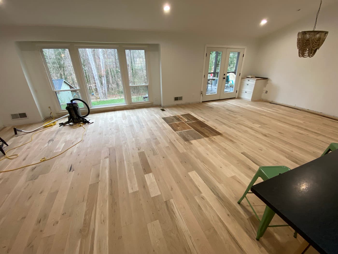 Bare engineered white oak floor in large living room with stain samples cut in and sanding equipment present, Oak Park Raleigh NC