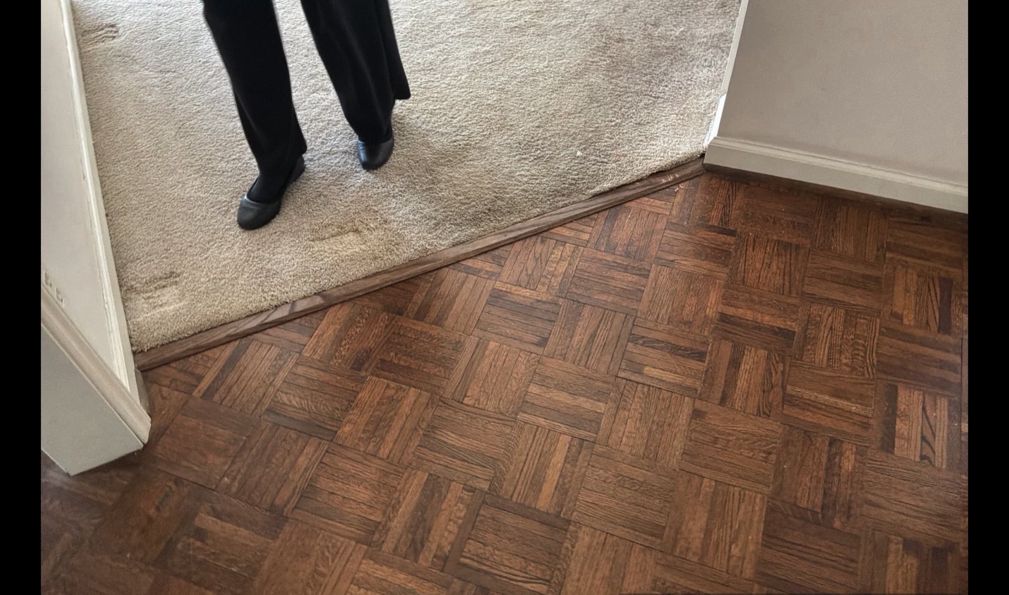 Original dark parquet flooring meeting worn carpet before renovation in Downtown Raleigh home