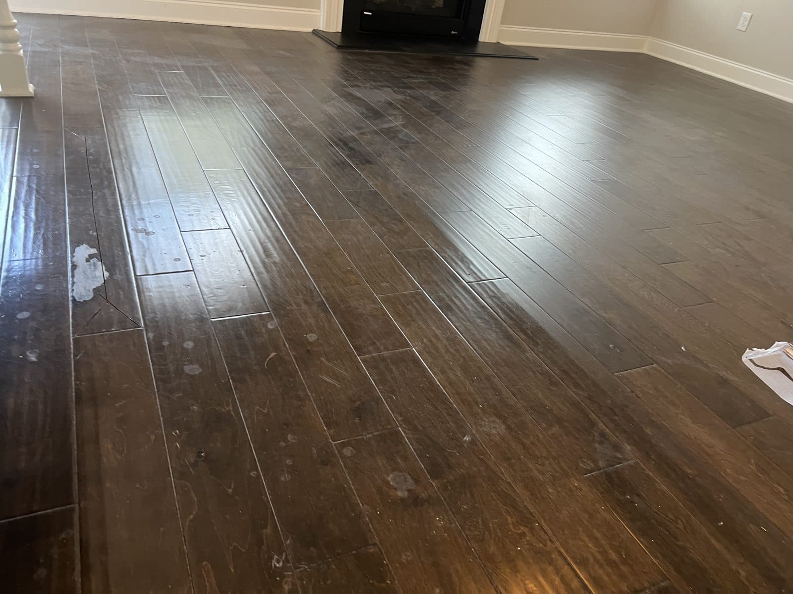 Gray, streaked polish buildup on a dark engineered floor in front of a fireplace before deep clean in Fuquay-Varina NC