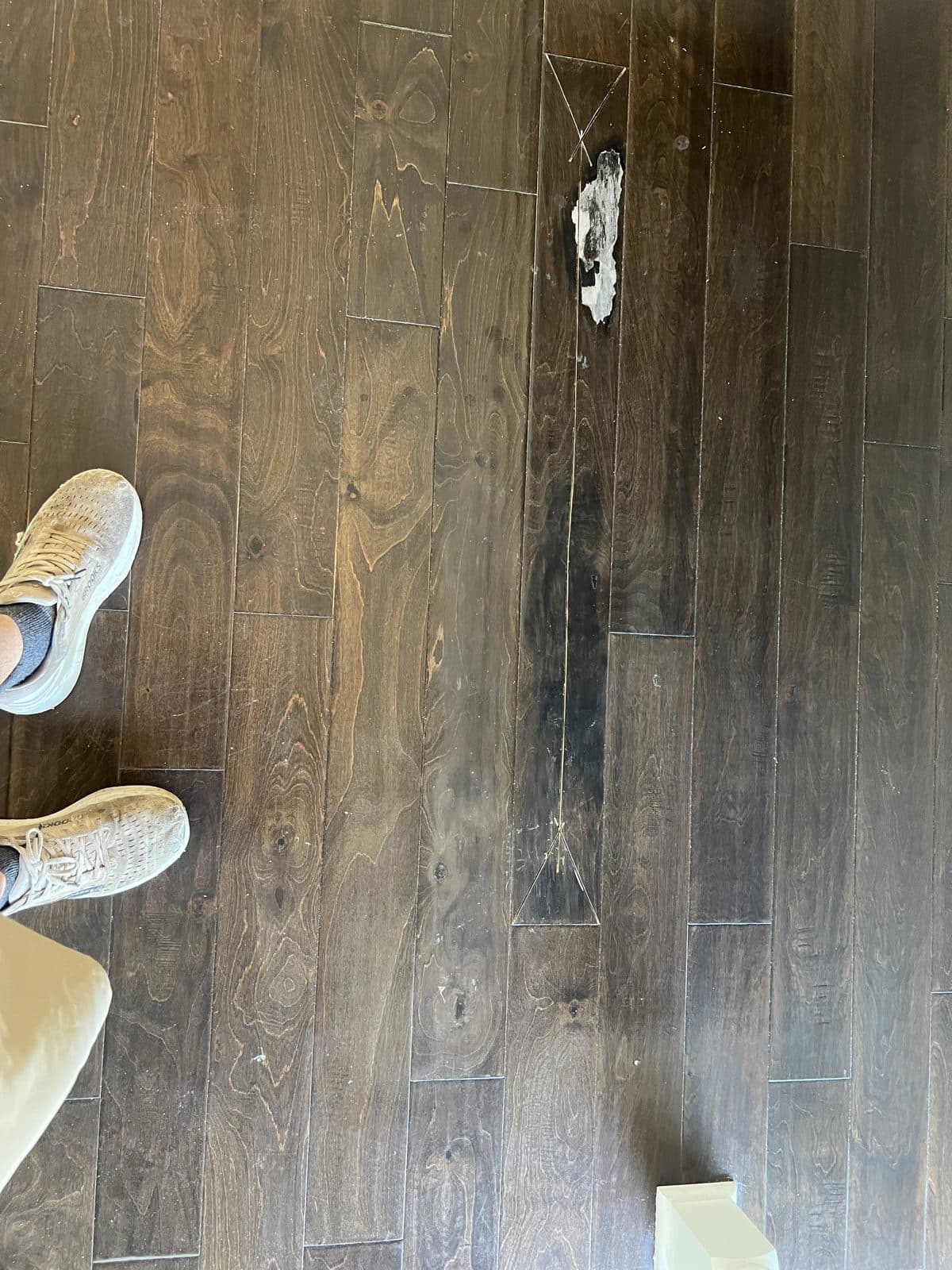 Damaged engineered floor board with chipped finish marked with tape for replacement in Fuquay-Varina NC