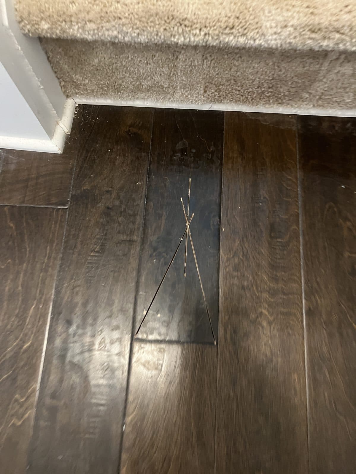 Damaged engineered board at the base of a carpeted stair marked for replacement in Fuquay-Varina NC