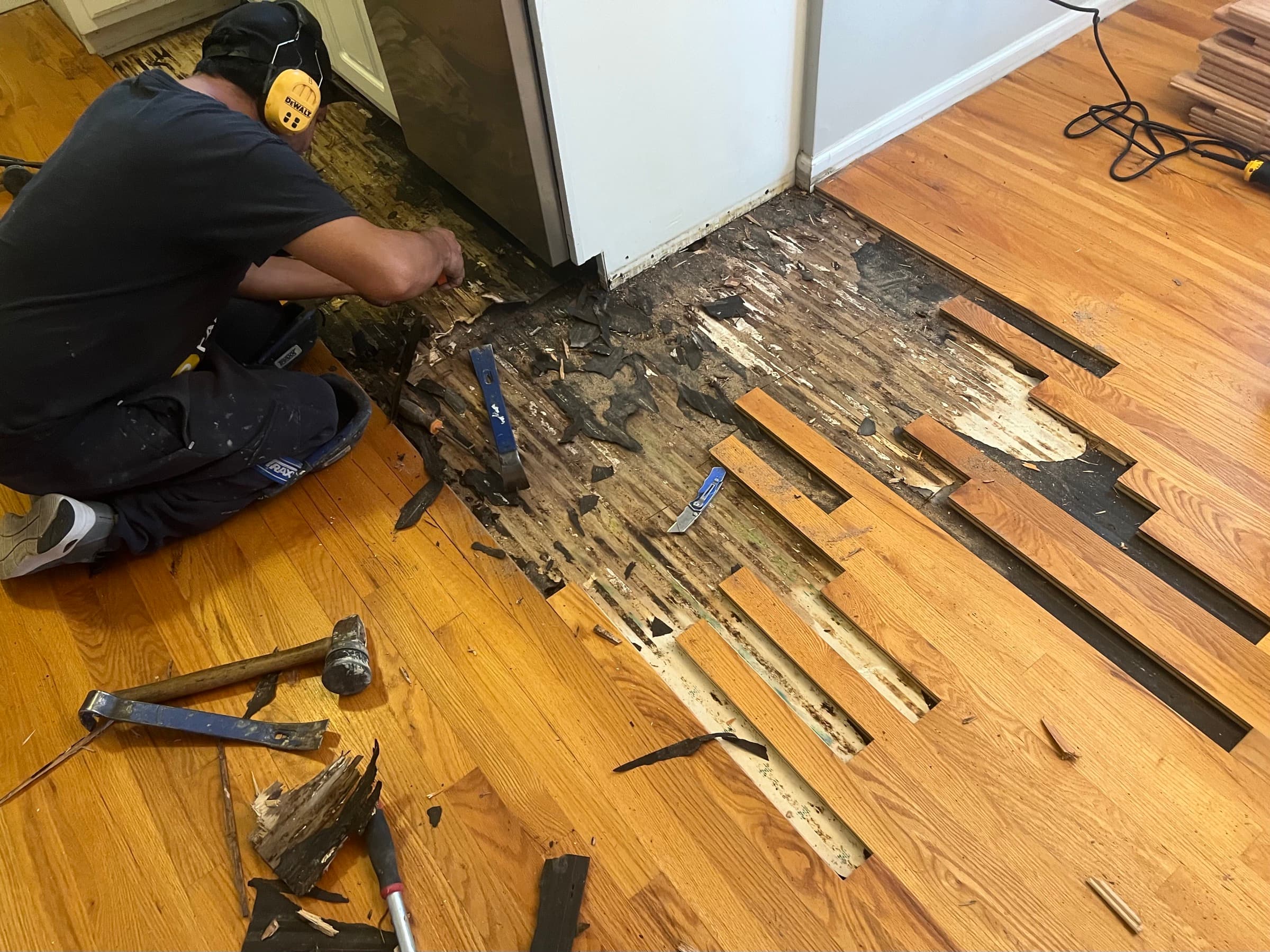 Rotted hardwood floor being demolished in Matthews Farm Clayton NC kitchen after dishwasher leak, damaged black boards and subfloor visible