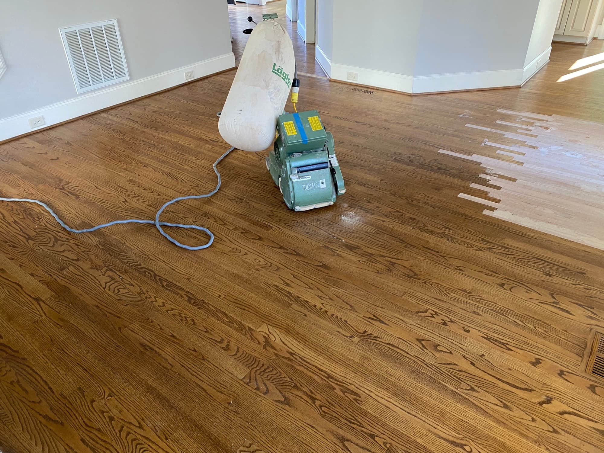 Lagler Hummel drum sander mid-pass on red oak floors in Hocutt Farm Clayton NC, lighter repair area visible at right