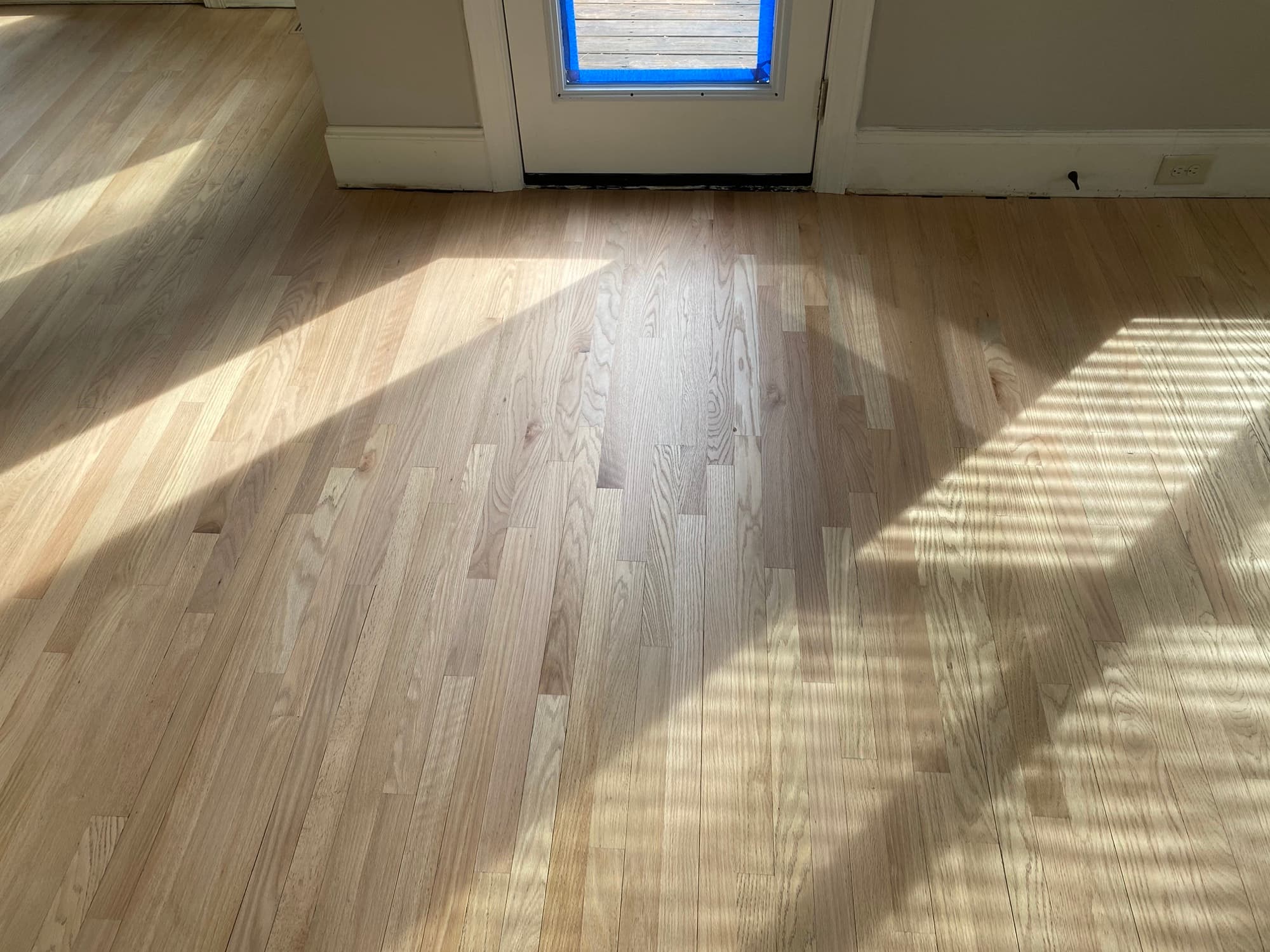 Entire red oak floor sanded bare in Hocutt Farm Clayton NC, back door wrapped in blue protective film, repair area fully integrated with existing floor