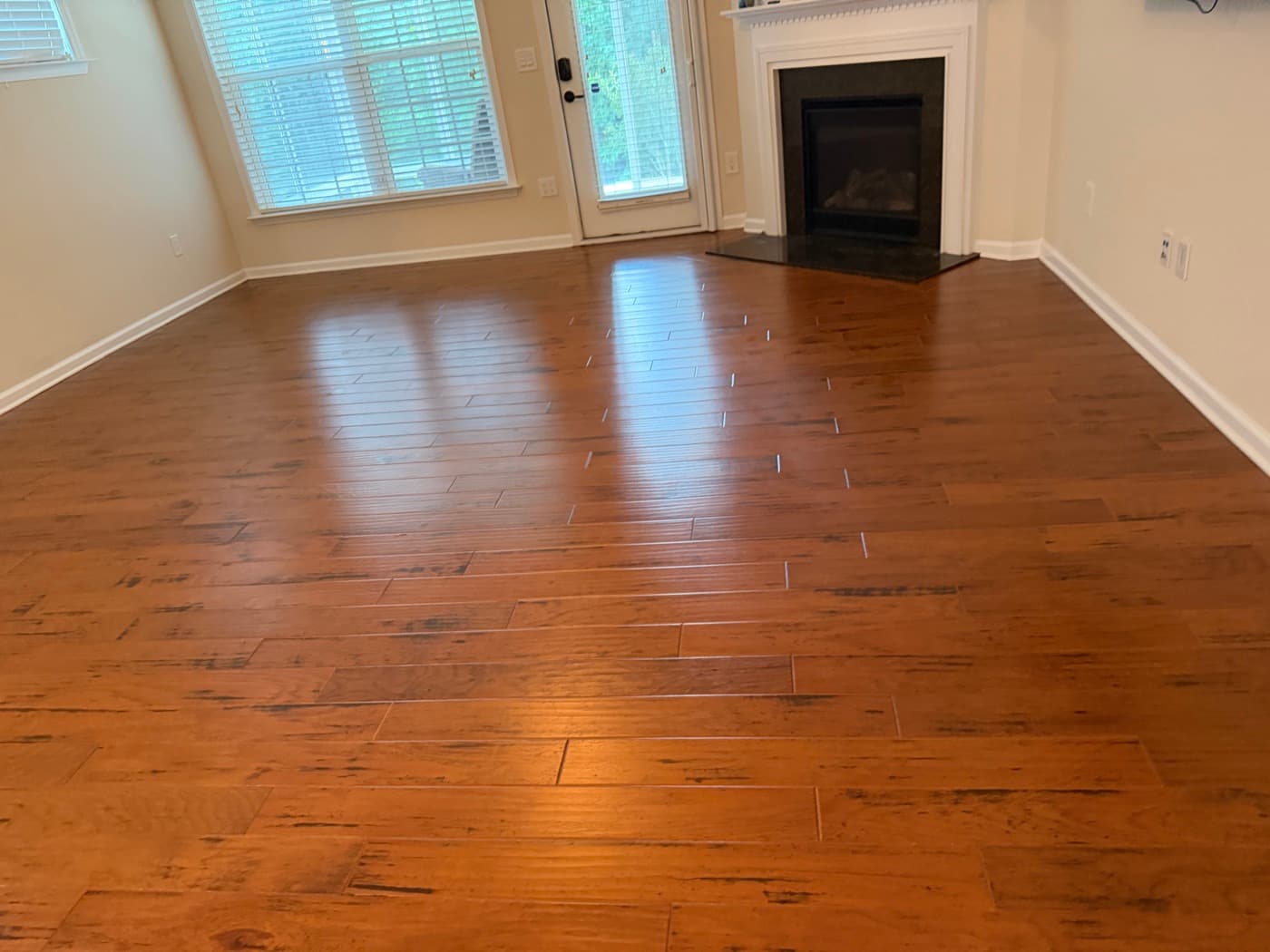 Hand-scraped hickory floor restored to original factory finish after polish removal and deep clean in Holly Springs NC, living room with corner gas fireplace