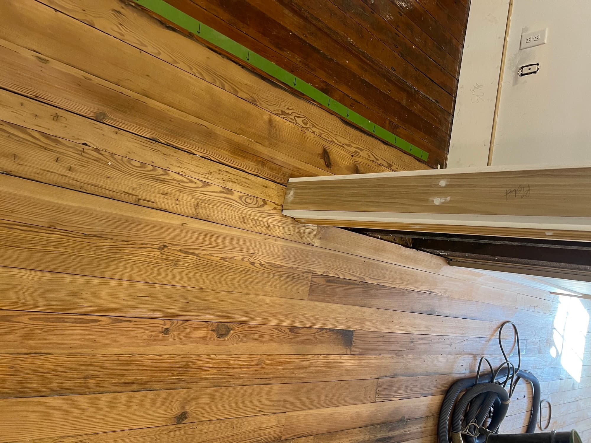 Junction of original and salvaged patched heart pine boards during refinishing in Morrisville NC, green masking tape marking repair boundary