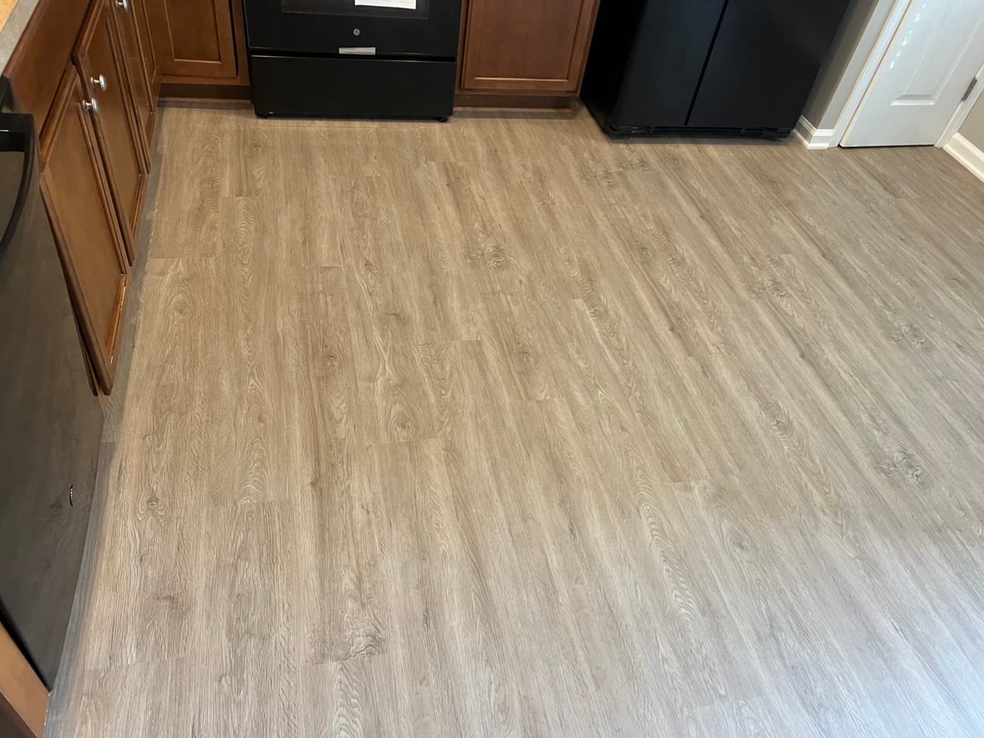 Close-up of finished LVP in kitchen area with wood cabinets and black appliances in Garner NC townhouse