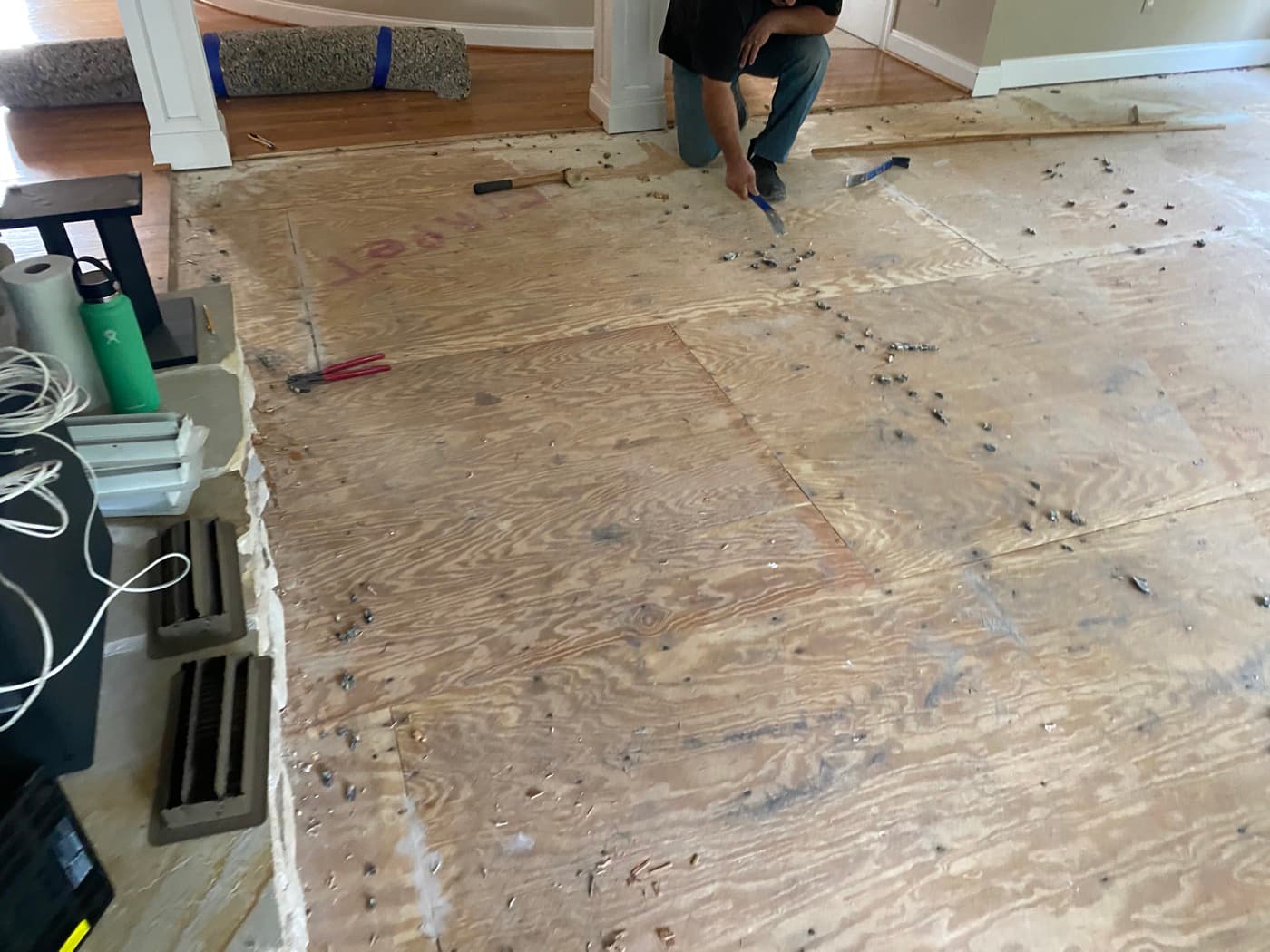 Carpet removed from family room, crew pulling carpet pad staples from plywood subfloor at Sunset Lakes Fuquay-Varina NC
