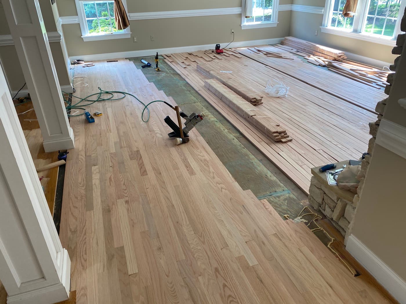 Wide view of family room red oak hardwood installation in progress with flooring nailer and boards laid out at Sunset Lakes Fuquay-Varina NC