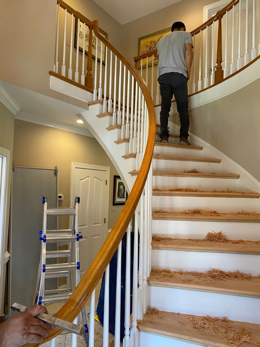 Worker hand scraping curved staircase treads to bare wood at Sunset Lakes Fuquay-Varina NC