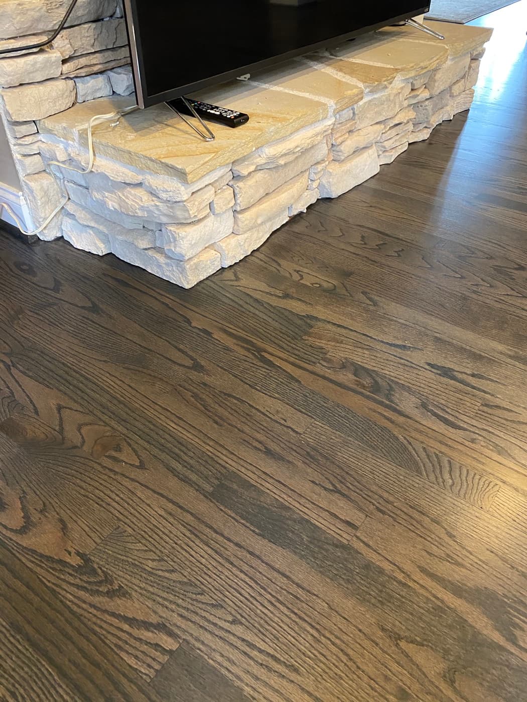 Finished Bona Driftwood stained red oak floor tight against stone fireplace base at Sunset Lakes Fuquay-Varina NC