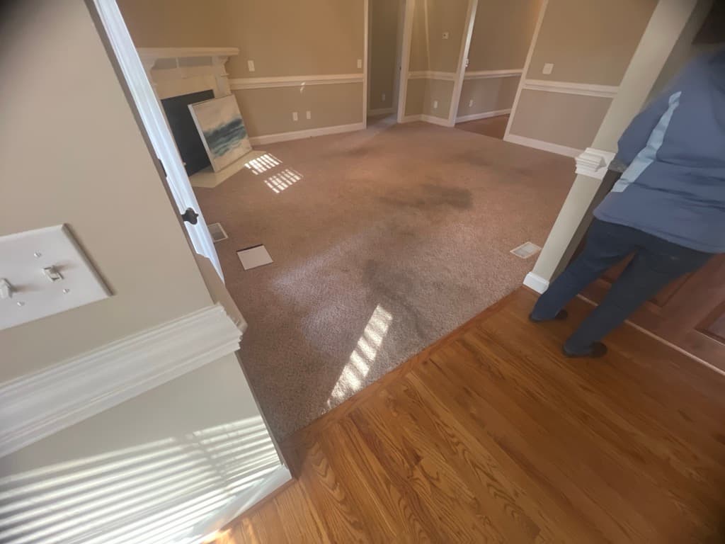 Family room with carpet before red oak installation in Summerset Place Clayton NC, existing hardwood visible at threshold
