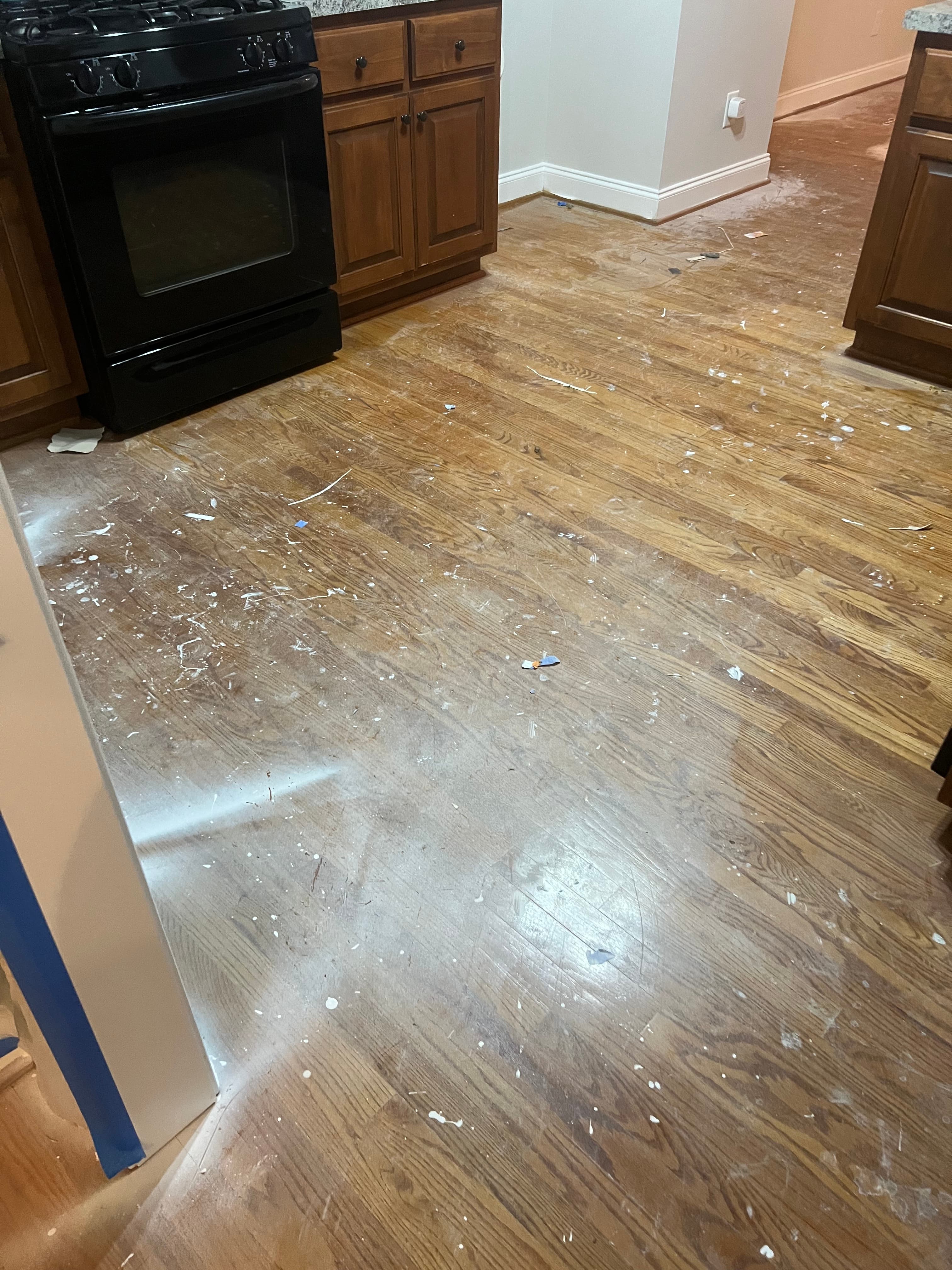 Existing red oak hardwood in breakfast nook before sanding in Summerset Place Clayton NC, worn finish with paint drips and debris