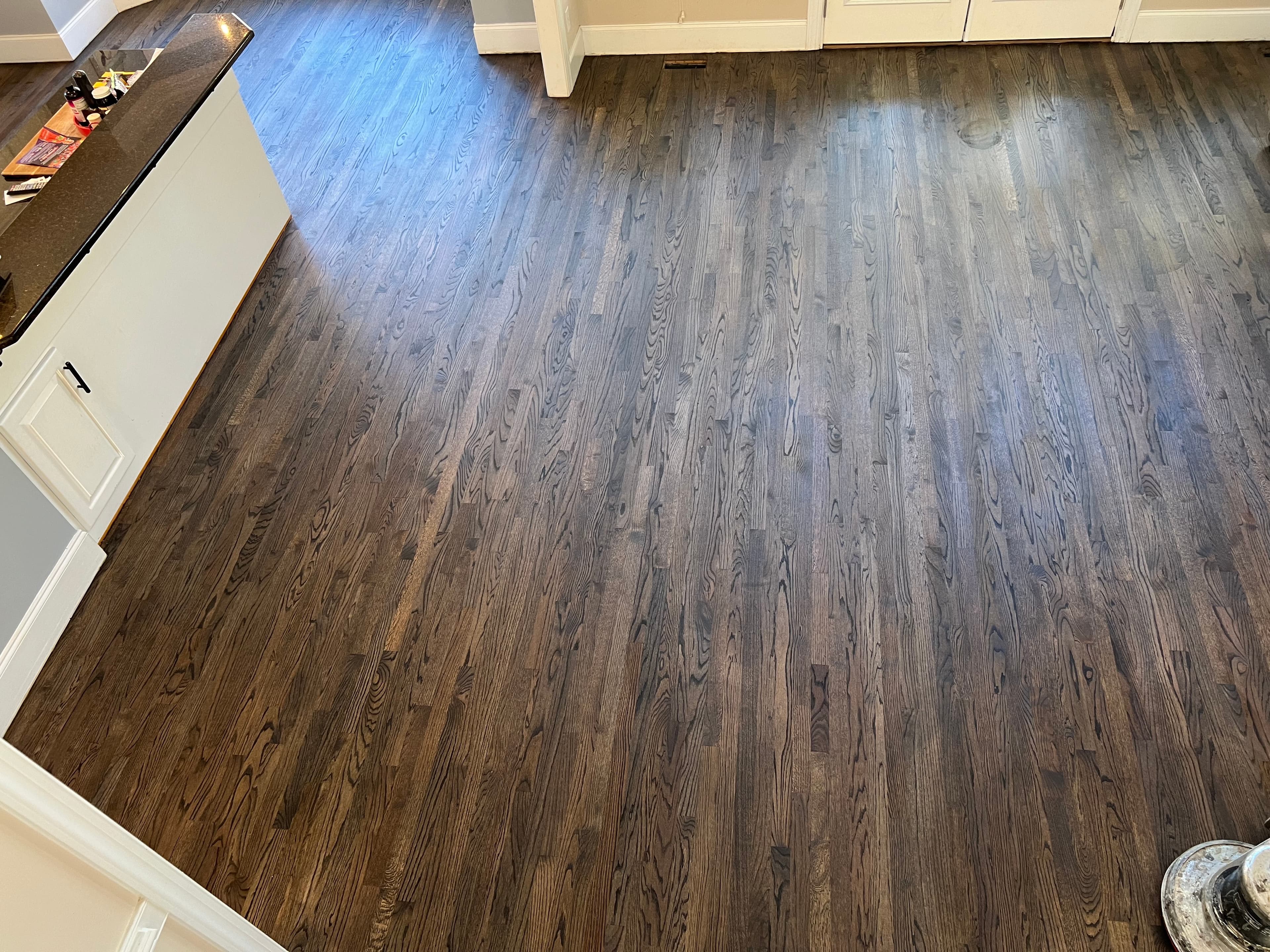 Finished red oak floors with custom hardwax oil blend in kitchen and living area in Austin Pond Clayton NC, very dark rich tone with white cabinetry and dark island