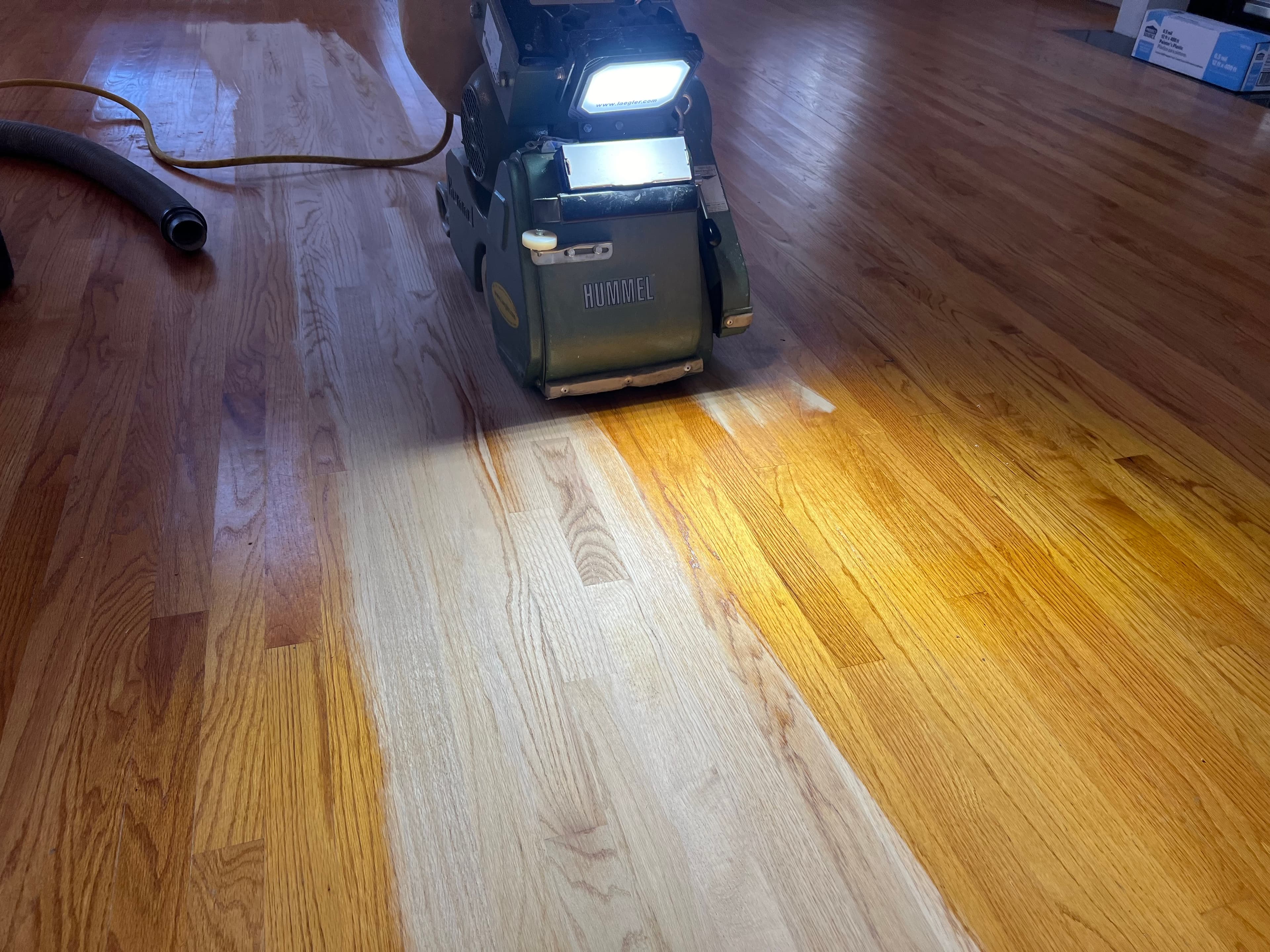 Lagler Hummel drum sander in action on red oak floor in Austin Pond Clayton NC, light illuminating contrast between sanded pale wood and remaining old finish