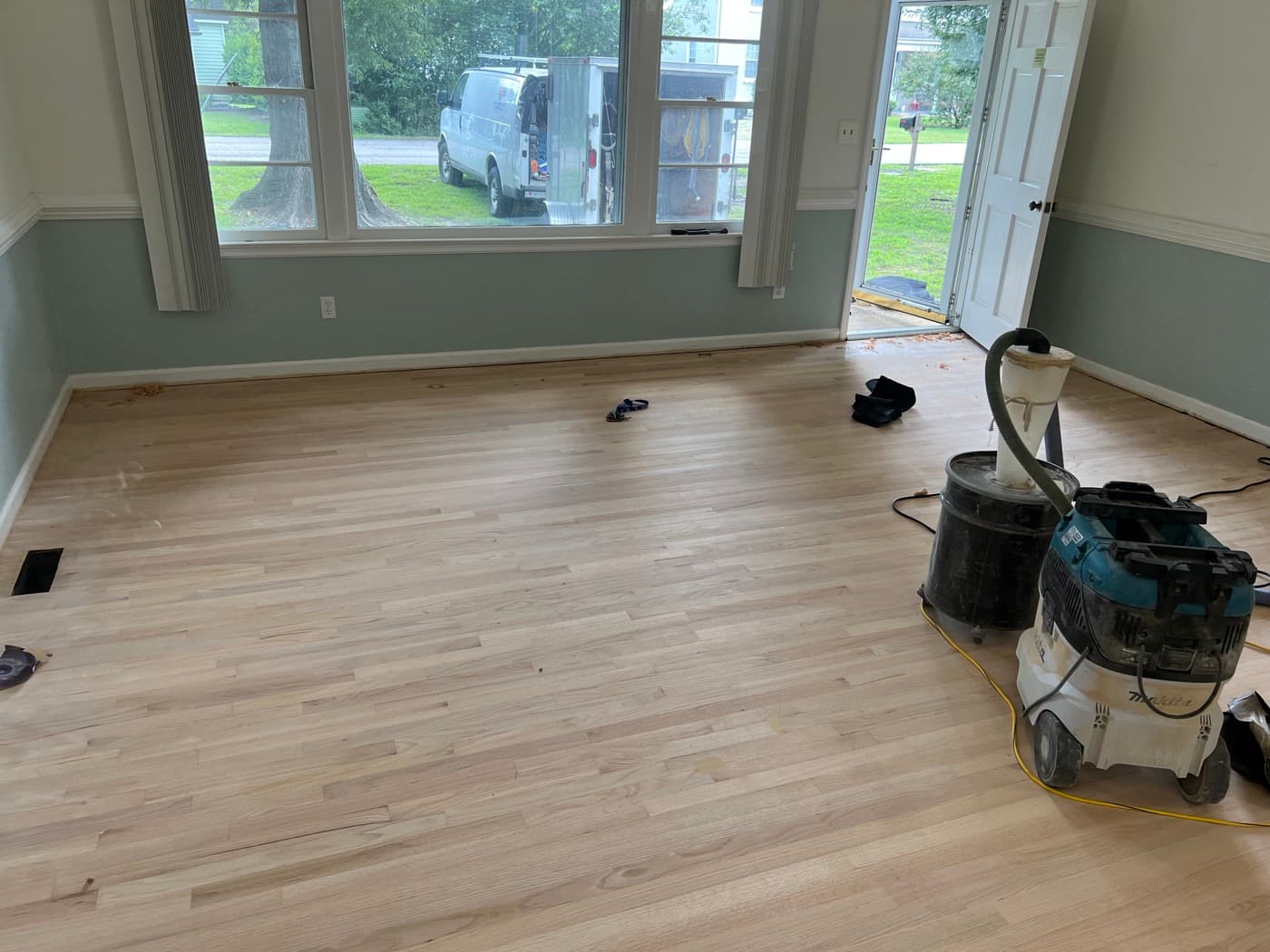 Red oak floor sanded bare in living room during refinishing in Downtown Knightdale NC, sanding equipment visible