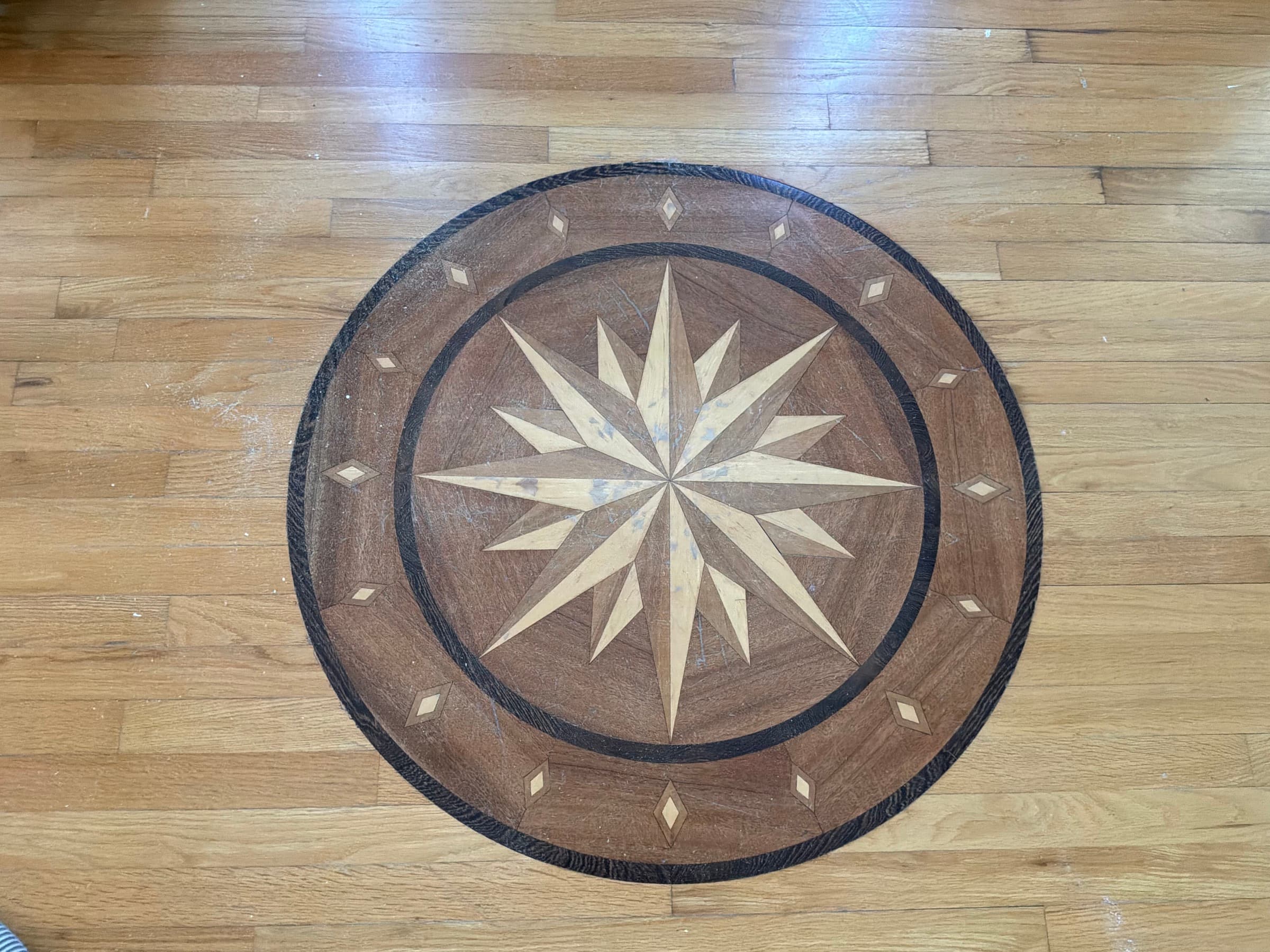 Compass rose medallion before refinishing, amber oil-based polyurethane on surrounding red oak floor in Glen Laurel Clayton NC