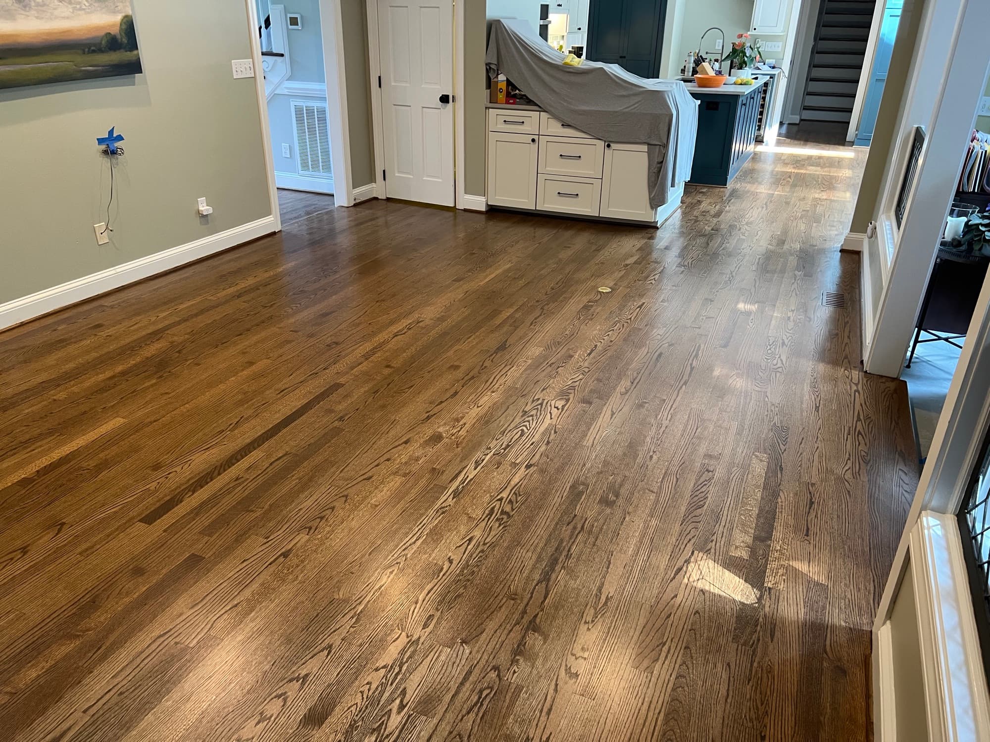 Finished custom stained red oak floors running through open plan living area in Lochmere Cary NC, looking toward kitchen with island draped