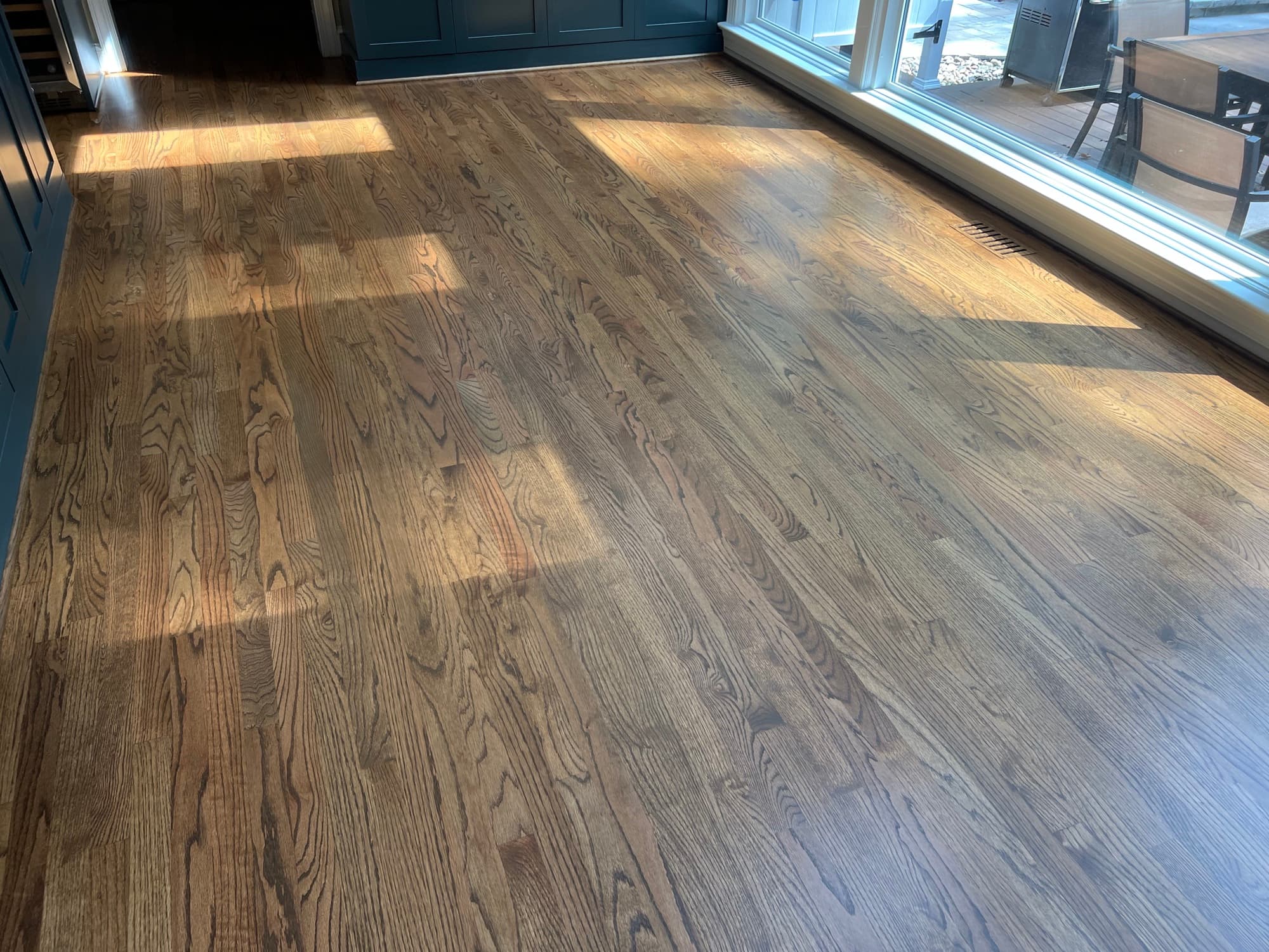 Finished red oak floors in raking afternoon light near sliding glass doors in Lochmere Cary NC, custom stain showing grain depth and warmth
