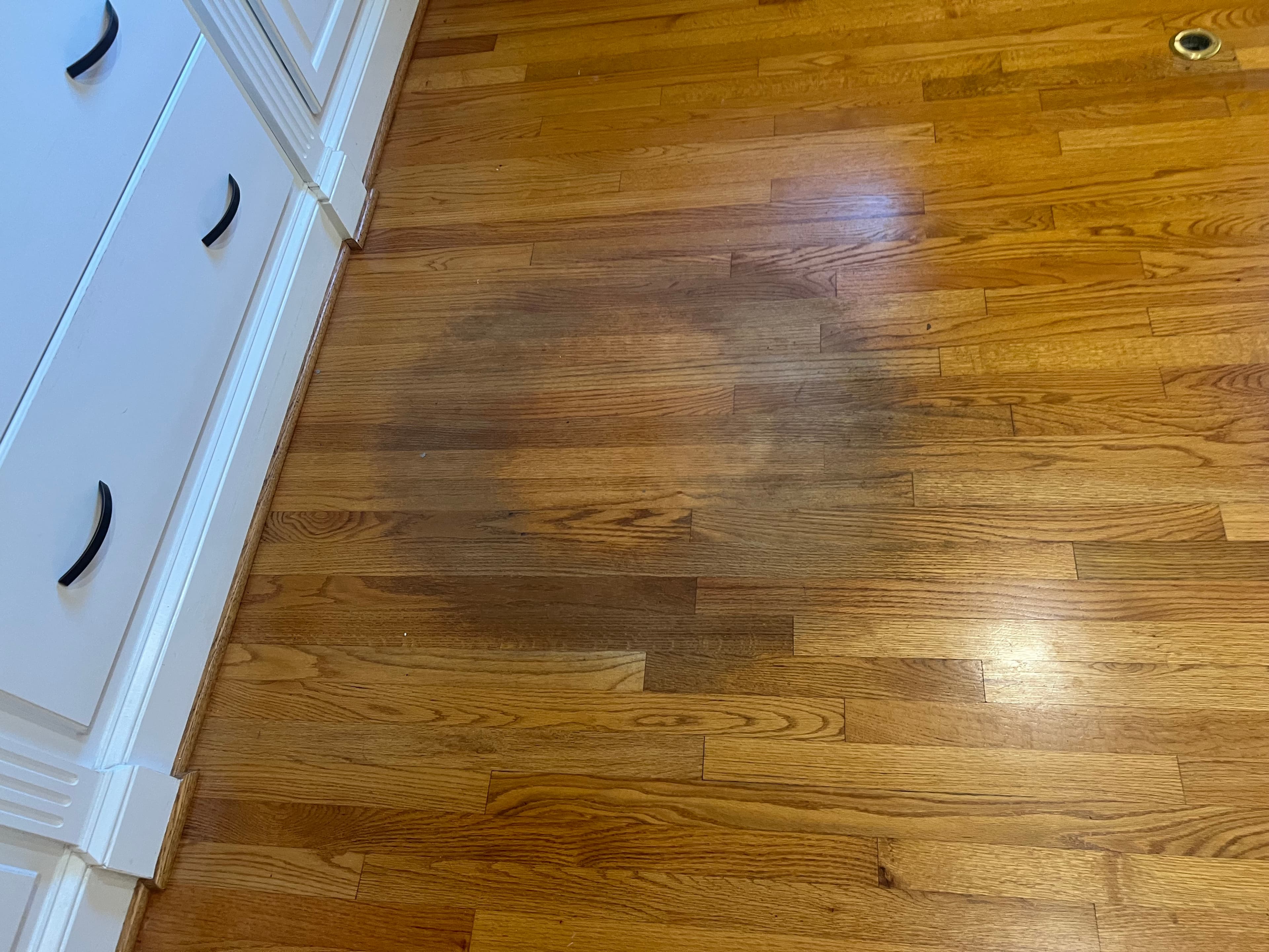 Worn 3.25 inch red oak floors before refinishing in Lochmere Cary NC, dark water stain patch visible near cabinet, old brass floor vent