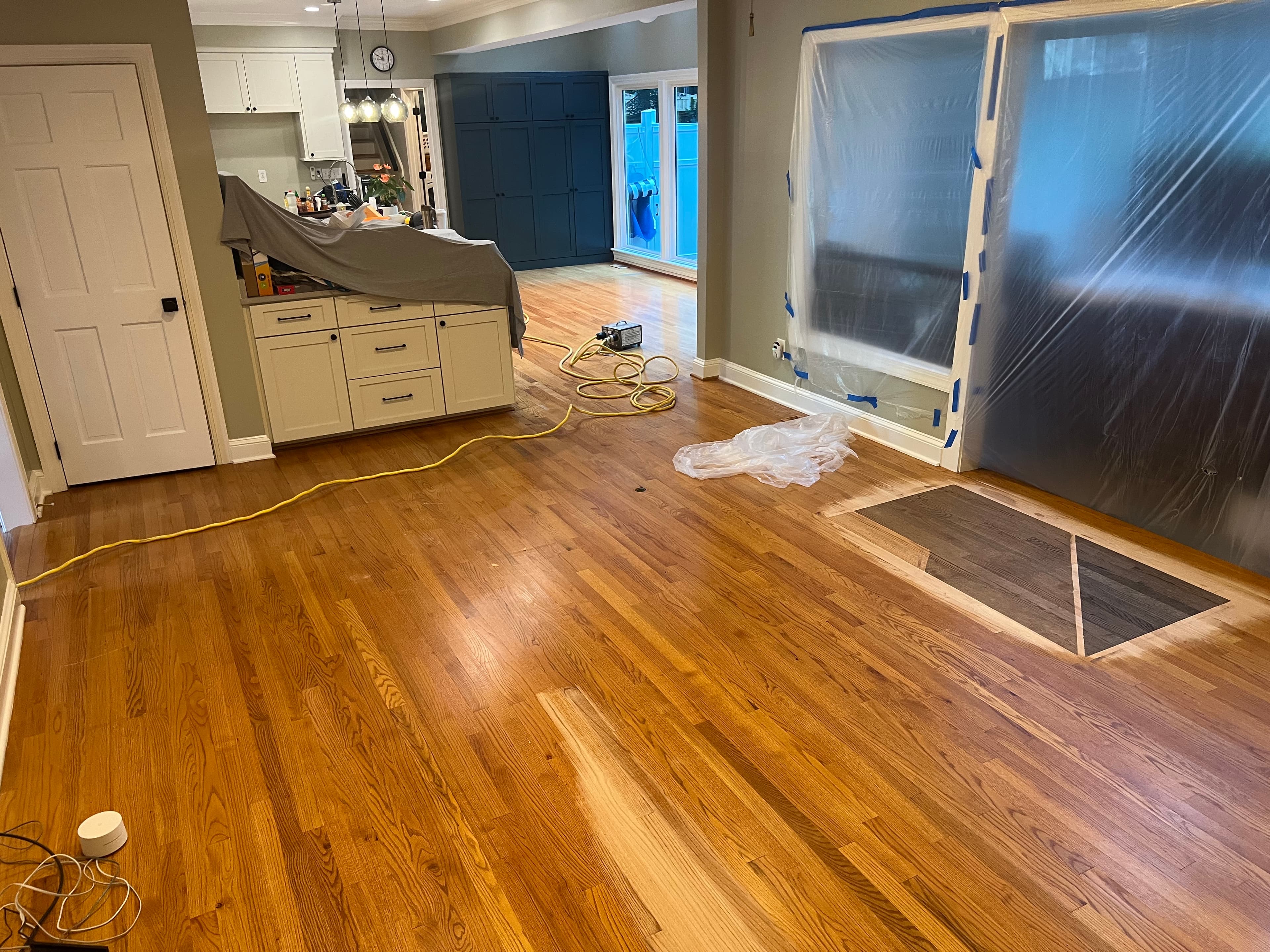 Mid-project red oak refinishing in Lochmere Cary NC, open plan living area with kitchen draped, flush-mount vent cutout visible in floor