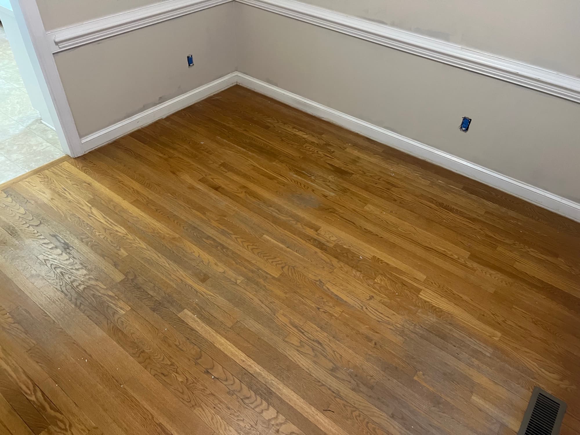 Heavily ambered red oak floors in corner room before refinishing in Wilson NC, orange cast from aged oil-based polyurethane, wainscoting visible
