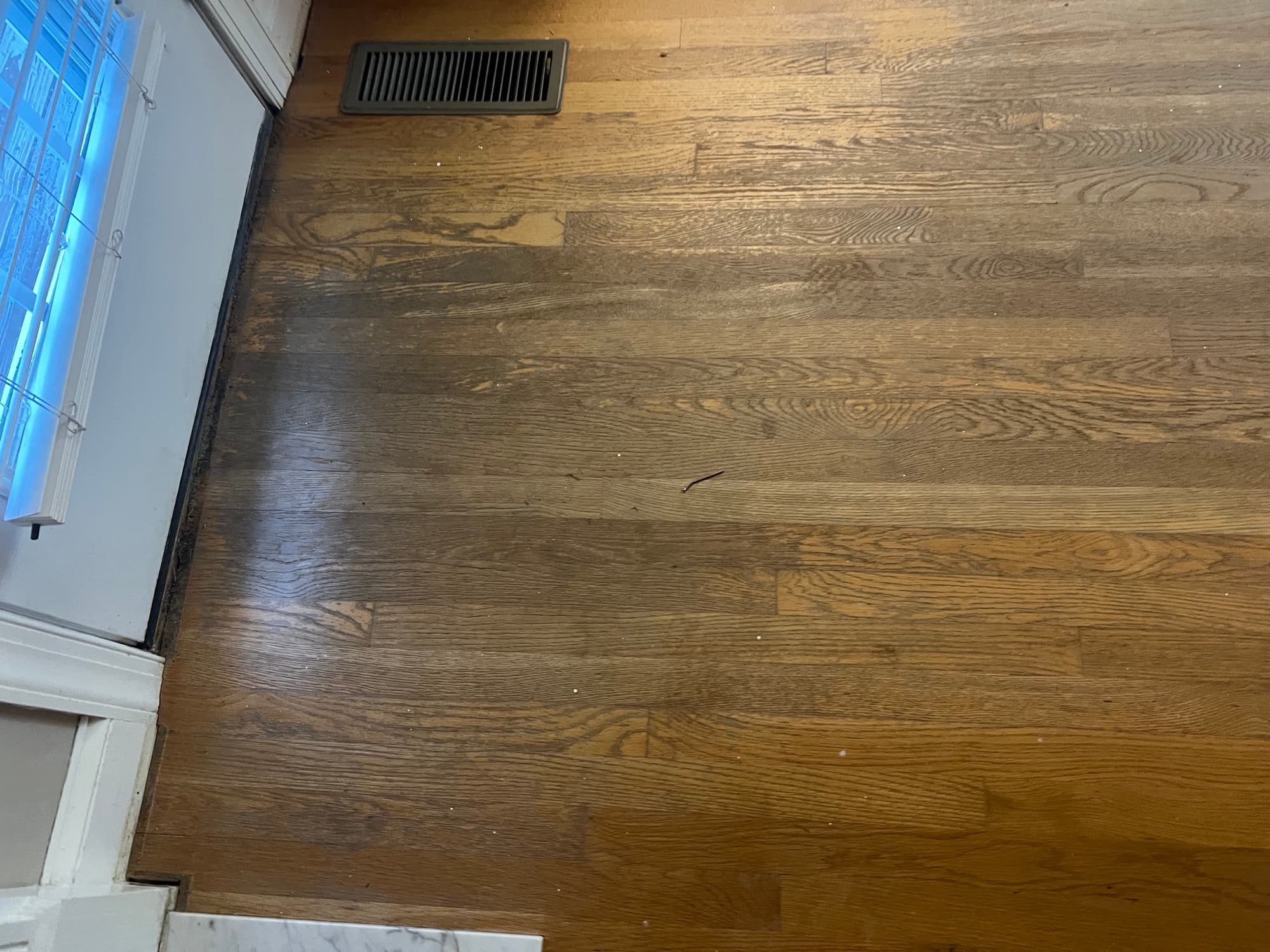 Worn and ambered red oak floors near window before refinishing in Wilson NC, heavy orange cast from aged oil-based polyurethane