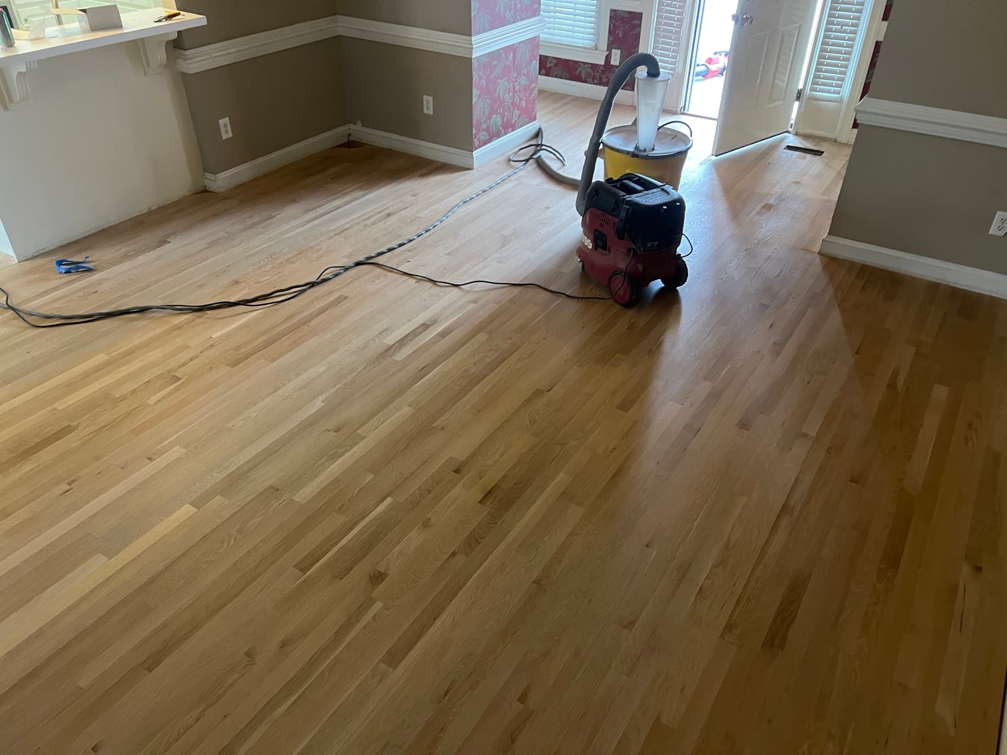 Red oak floors sanded back to bare pale wood in Wilson NC living room, Festool vacuum in frame, French doors in background