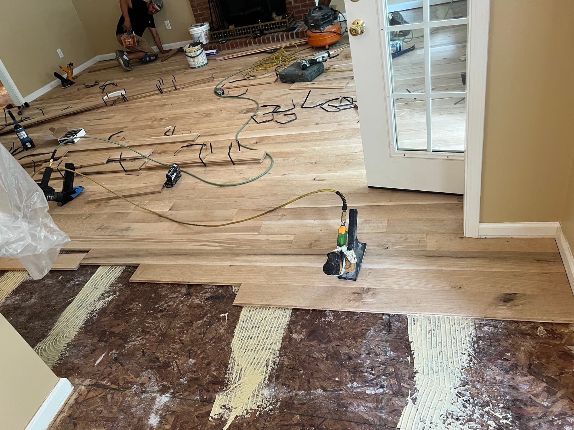 White oak hardwood installation spreading across living room in Westlake Wendell NC, adhesive and nailer visible