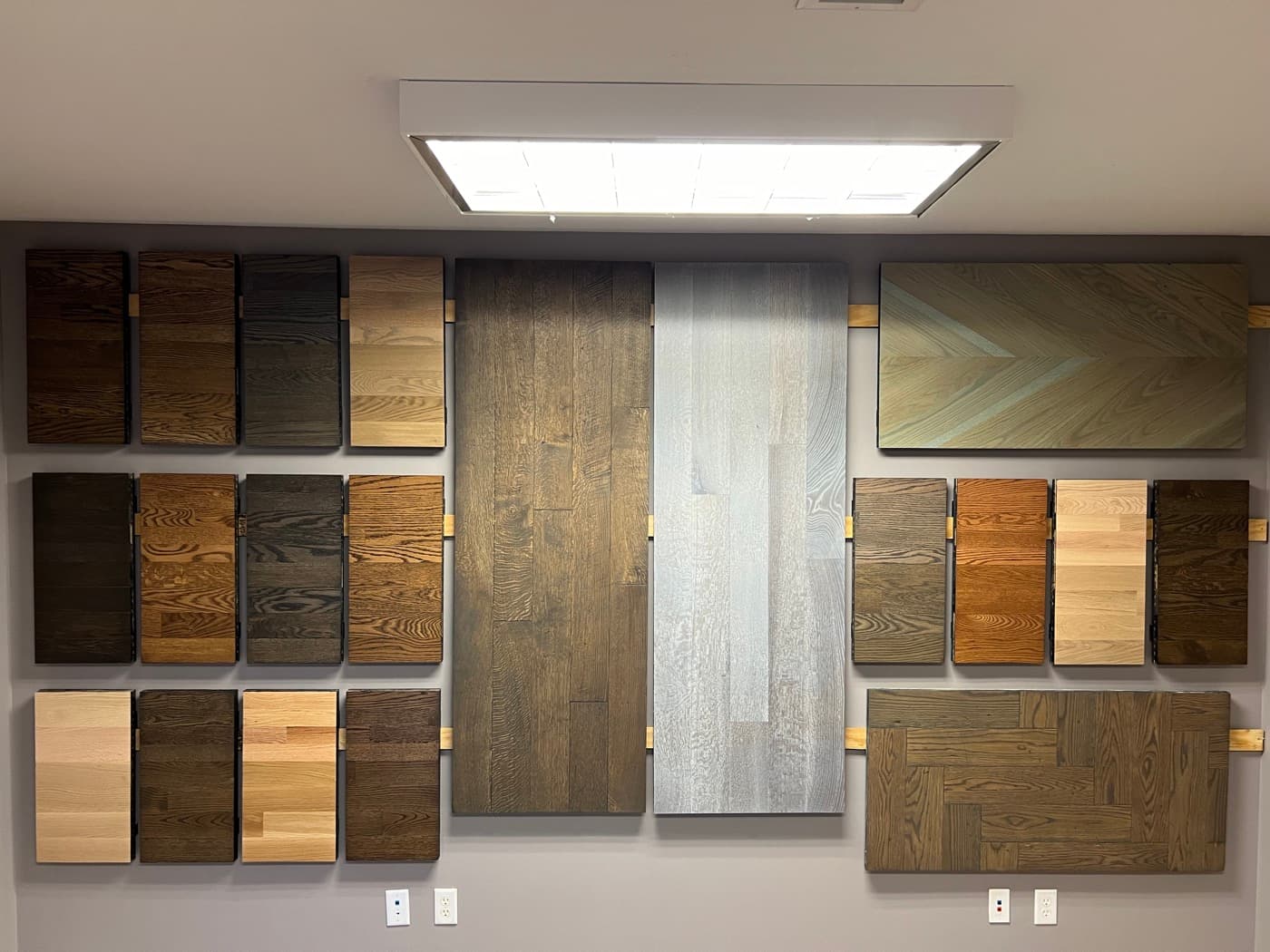 Pre-made stain and finish sample boards displayed on the wall at 12th And Oak Floor Co. showroom in Clayton NC