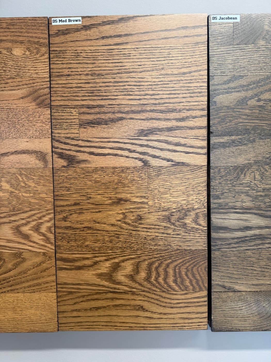 DuraSeal Medium Brown and DuraSeal Jacobean side by side on showroom wall boards: top half red oak, bottom half white oak