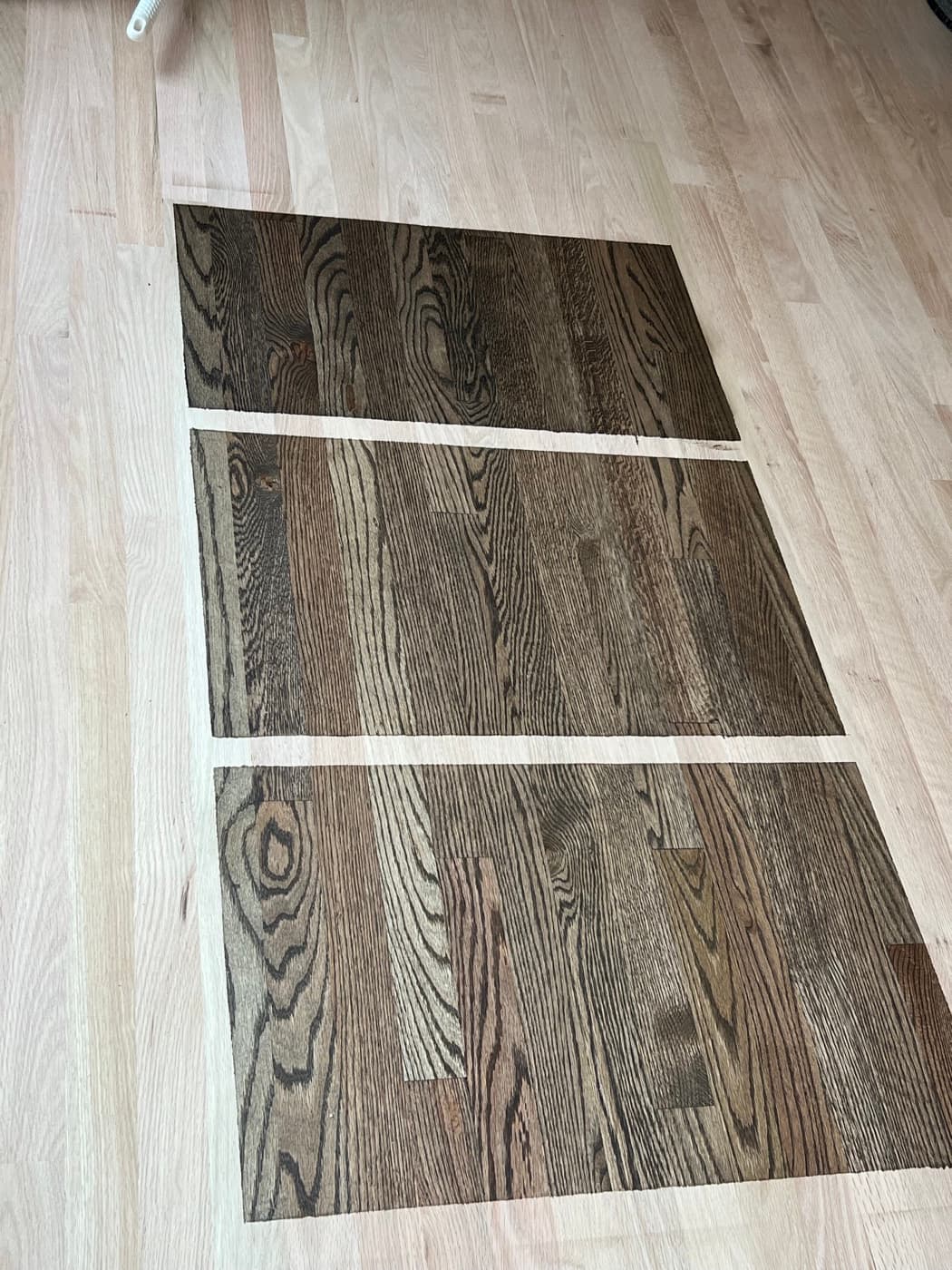 Multiple dark hardwax oil custom blend samples on white oak wide plank showing color range from warm charcoal to near-black
