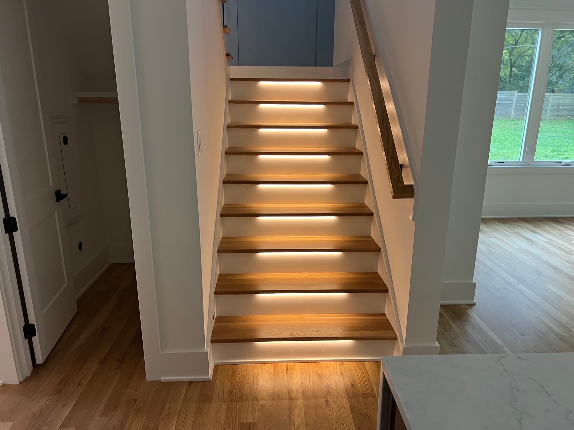 Staircase remodeling with white oak treads, white risers, and LED under-tread lighting in Raleigh NC matching hardwood floors throughout