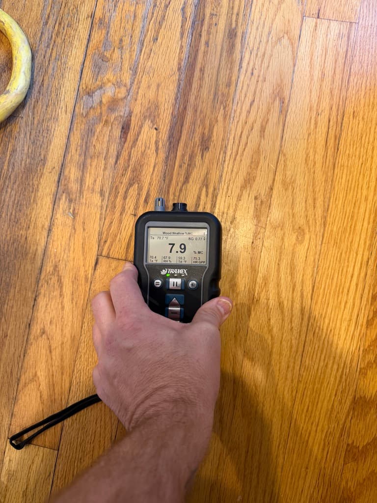 Tramex pinless moisture meter reading 7.9 percent on a red oak floor