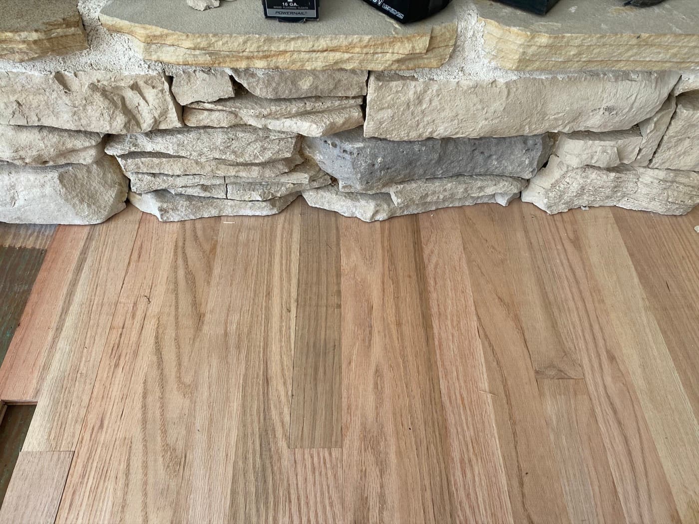Red oak boards slid under undercut stone fireplace base for a seamless zero-gap fit at Sunset Lakes Fuquay-Varina NC
